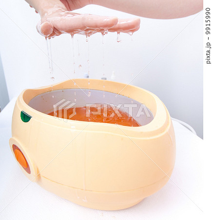 Female hand orange parrafin wax in bowl. Manicure beauty spa salon Female hand orange parrafin wax in bowl. Manicure beauty spa salon 9915990