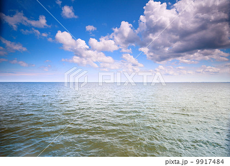 Cloudy blue sky above a surface of the sea 9917484