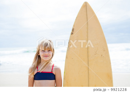 Smiling young girl standing next to surfboard 9921228