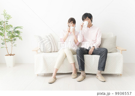 ソファーに座り、コーヒーを飲みながら会話をするカップル ソファーに座り、コーヒーを飲みながら会話をするカップル 9936557