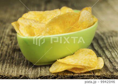 Crispy potato chips in green bowl on wooden boards Crispy potato chips in green bowl on wooden boards 9942046