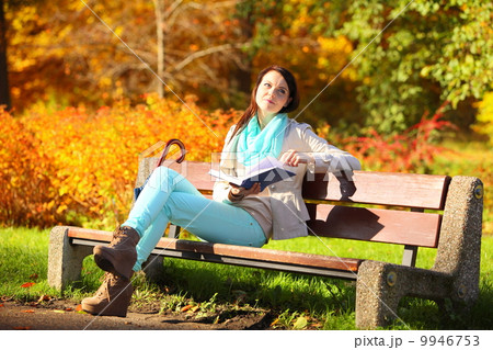 Young girl relaxing in autumnal park reading book 9946753