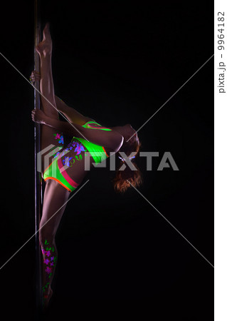 Flexible girl dancing on pole under UV light 9964182