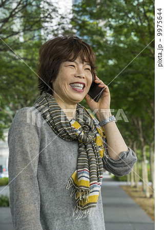 Portrait of an elderly woman using cellphone in a park in an asian city on a sunny day. Half Body. 9975644