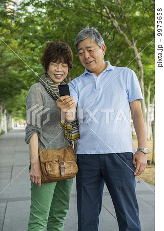 Portrait of an elderly couple traveller taking photos in a park with in an asian city on a sunny day 9975658