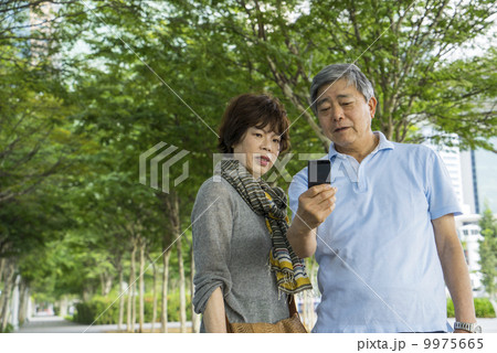 Portrait of an elderly couple traveller taking photos in a park with in an asian city on a sunny day 9975665
