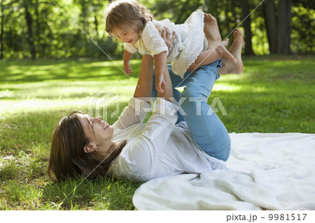 A mother lying on her back with her twin daughter balancing on her knees, outdoors. A mother lying on her back with her twin daughter balancing on her knees, outdoors. 9981517