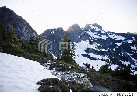 A young man hikes around a snow patch while going to the summit of a large mountain in the Cascades of Washington, USA. A young man hikes around a snow patch while going to the summit of a large mountain in the Cascades of Washington, USA. 9981611