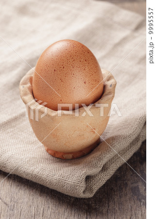 brown egg in handmade holder on rustic table brown egg in handmade holder on rustic table 9995557