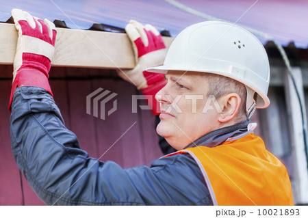 Carpenter with a wooden board near the roof 10021893