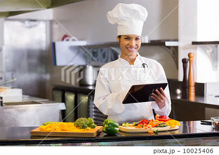 Smiling chef using digital tablet while cutting vegetables Smiling chef using digital tablet while cutting vegetables 10025406