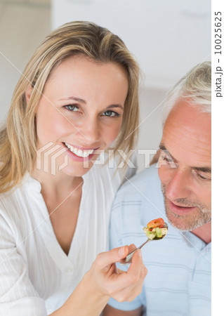 Happy woman feeding her partner a spoon of vegetables 10025625