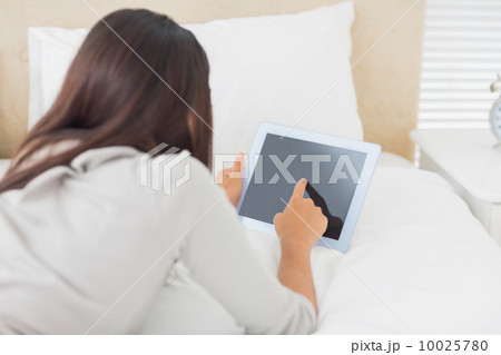 Young girl lying on her bed using her tablet 10025780