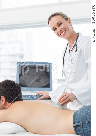 Doctor performing ultrasound scan on back of patient 10025880