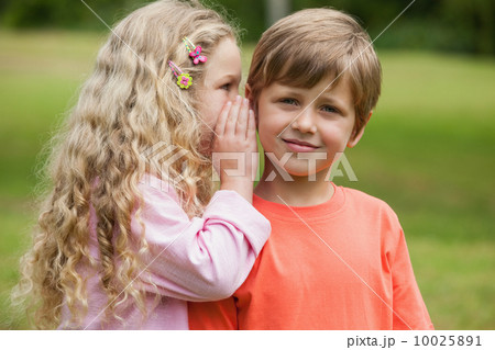 Girl whispering secret into boy's ear at park 10025891