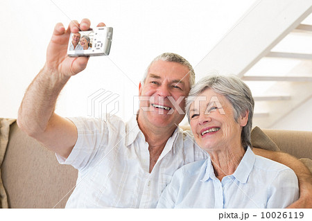 Senior couple sitting on couch taking a selfie 10026119