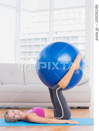 Smiling blonde holding exercise ball between legs 10026286