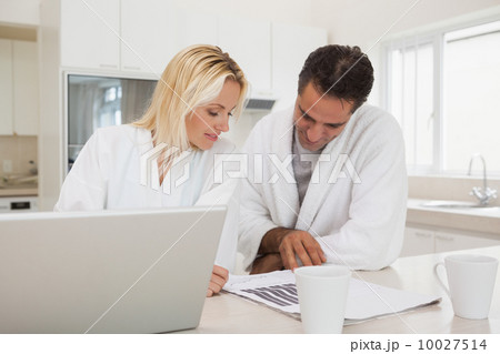 Casual business couple with laptop looking at graphs in kitchen Casual business couple with laptop looking at graphs in kitchen 10027514