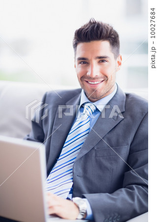 Happy businessman sitting on sofa using his laptop Happy businessman sitting on sofa using his laptop 10027684