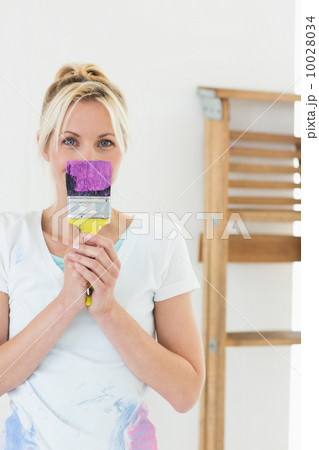 Woman holding paint brush in front of face at new house Woman holding paint brush in front of face at new house 10028034