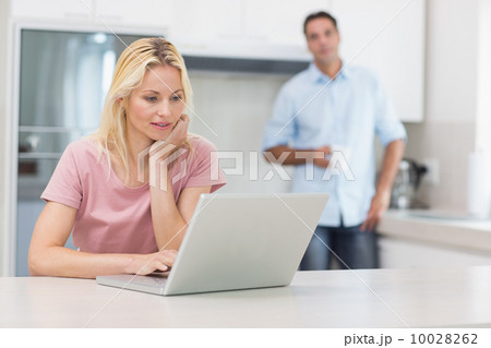 Woman using laptop with man drinking coffee in kitchen Woman using laptop with man drinking coffee in kitchen 10028262