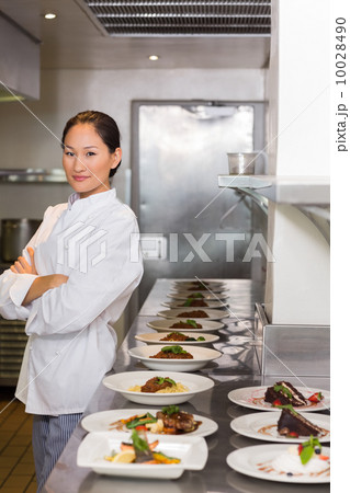 Confident chef besides cooked food in row at kitchen Confident chef besides cooked food in row at kitchen 10028490
