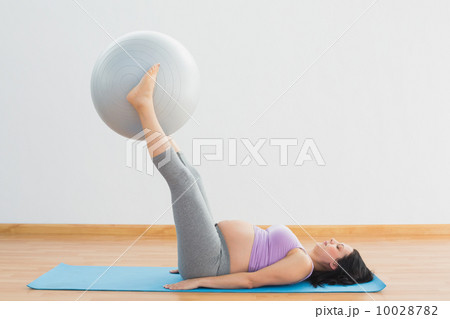 Happy pregnant woman lifting exercise ball with legs 10028782
