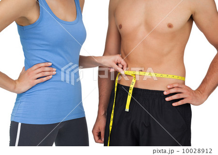 Mid section of a fit woman measuring mans waist 10028912
