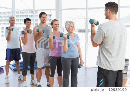 Class exercising with dumbbells in gym 10029199