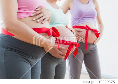 Pregnant women standing with red bow around bumps Pregnant women standing with red bow around bumps 10029375