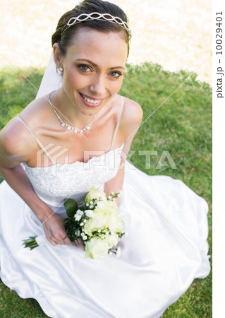 Bride holding flower bouquet while sitting on grass Bride holding flower bouquet while sitting on grass 10029401