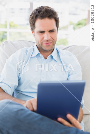 Focused man sitting on the couch using his tablet Focused man sitting on the couch using his tablet 10029512