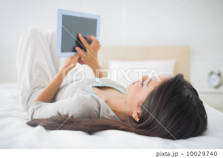 Young girl lying on bed looking at her tablet pc Young girl lying on bed looking at her tablet pc 10029740