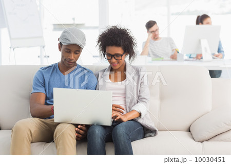 Couple using laptop with colleagues in background at creative of 10030451