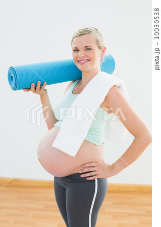 Pregnant blonde smiling at camera holding exercise mat 10030538
