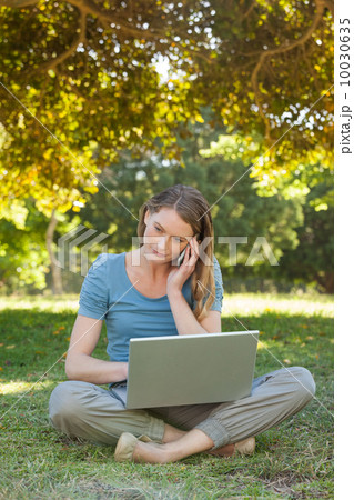 Relaxed woman using laptop and mobile phone at park 10030635