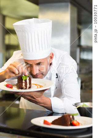 Concentrated male pastry chef decorating dessert in kitchen 10030771