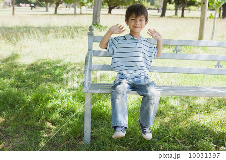 Happy young boy sitting on bench at park Happy young boy sitting on bench at park 10031397