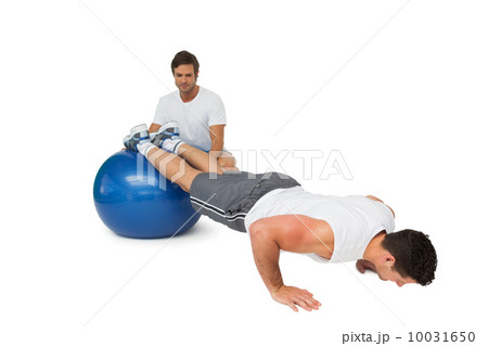 Male trainer helping young man exercise on fitness ball Male trainer helping young man exercise on fitness ball 10031650