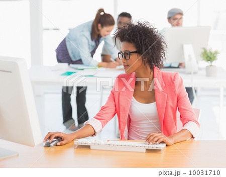 Female artist using computer with colleagues in background at of Female artist using computer with colleagues in background at of 10031710