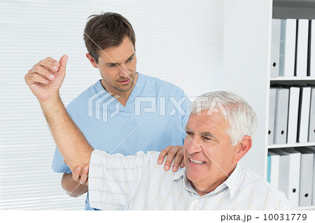 Physiotherapist assisting senior man to stretch his hand 10031779
