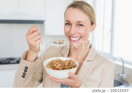 Happy businesswoman eating cereal before work in the morning Happy businesswoman eating cereal before work in the morning 10032097