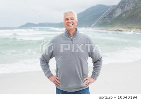 Happy senior man with hands on hips at beach Happy senior man with hands on hips at beach 10040194