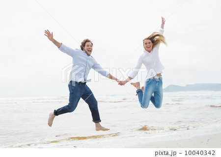 Cheerful couple holding hands and jumping at beach 10040342