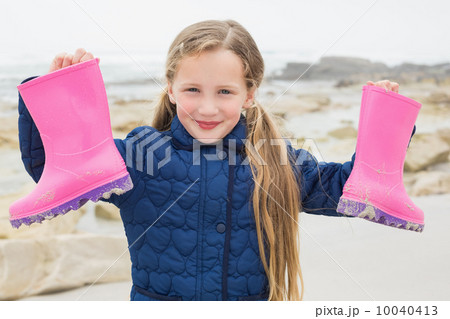 Cute smiling girl holding her wellington boots at beach Cute smiling girl holding her wellington boots at beach 10040413