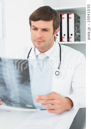 Concentrated male doctor looking at x-ray picture of spine Concentrated male doctor looking at x-ray picture of spine 10041030