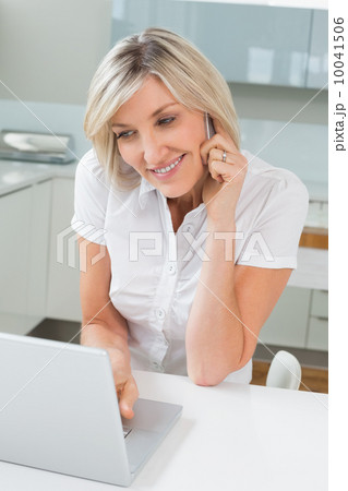 Casual woman using laptop while on call in kitchen Casual woman using laptop while on call in kitchen 10041506