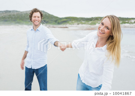 Smiling casual couple holding hands at beach 10041867
