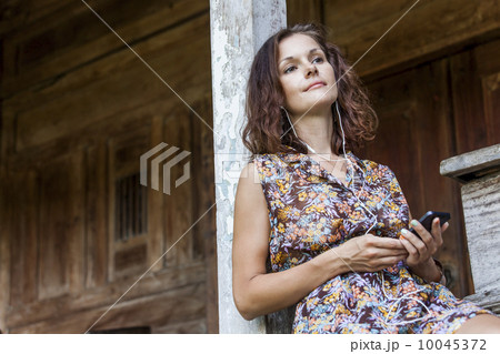 A young brunette caucasian woman Sitting and listening to music on her phone in a country house 10045372
