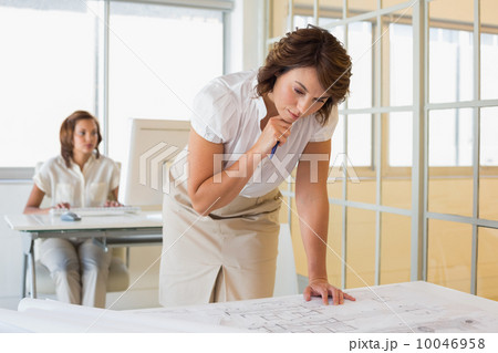 Businesswoman working on blueprints with colleague in background 10046958